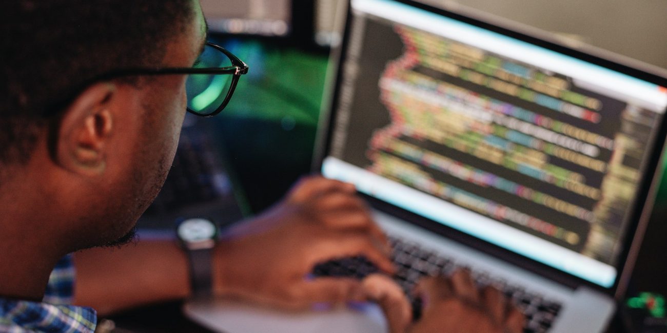 Black male in front of computer screen coding mobile app, web development, computer programming